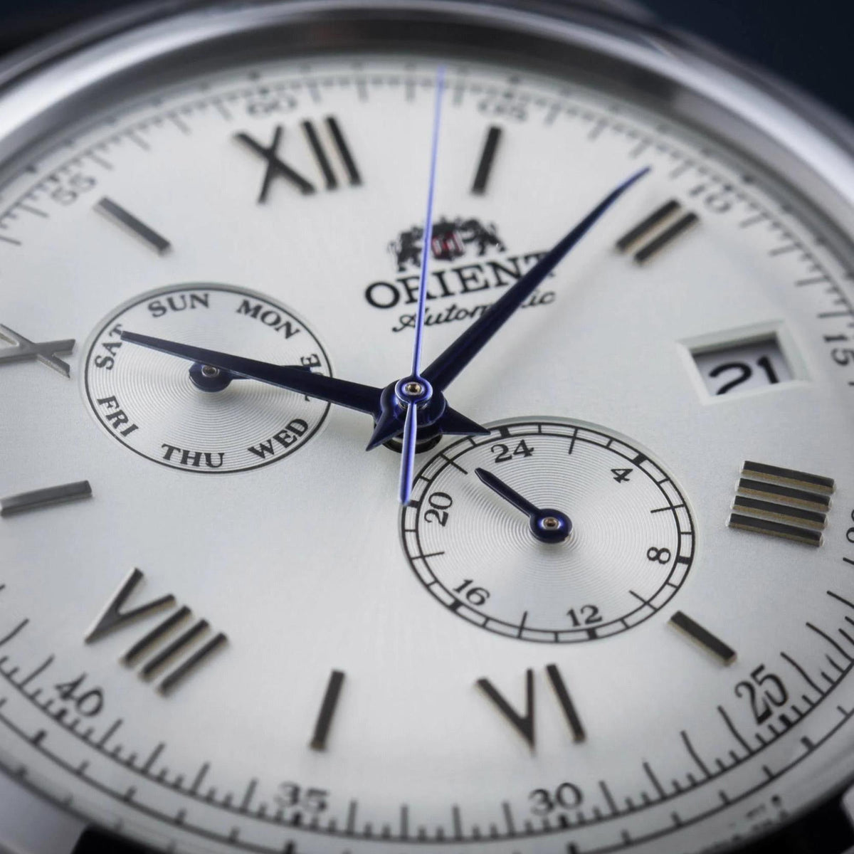 Men's wristwatch dial close-up with white background, blue hands, and a date window.