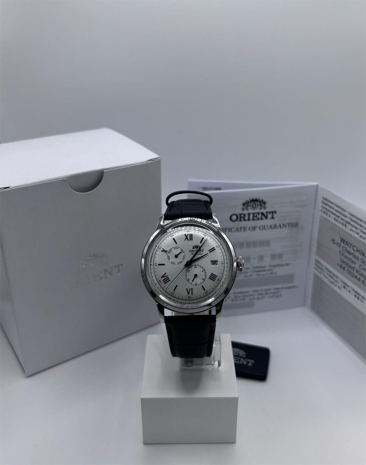 Men's automatic day-date watch with black leather strap and silver-tone case on stand