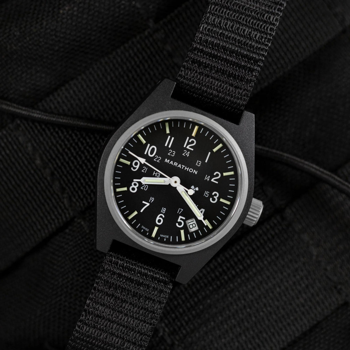 Close-up of black dial watch with Arabic numerals, date window, and black fabric strap
