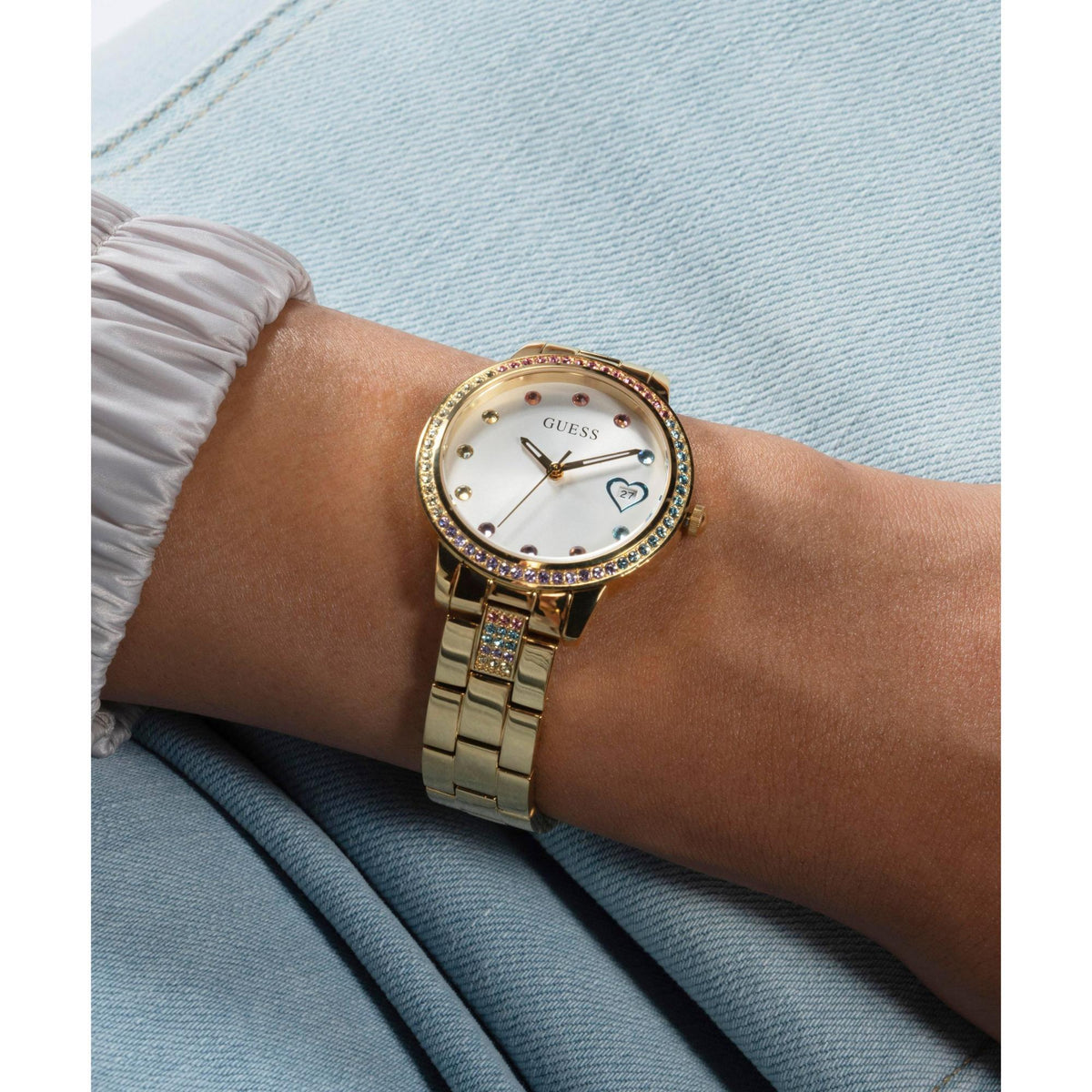 Gold tone ladies wristwatch with white dial and crystal bezel on metal bracelet on denim.