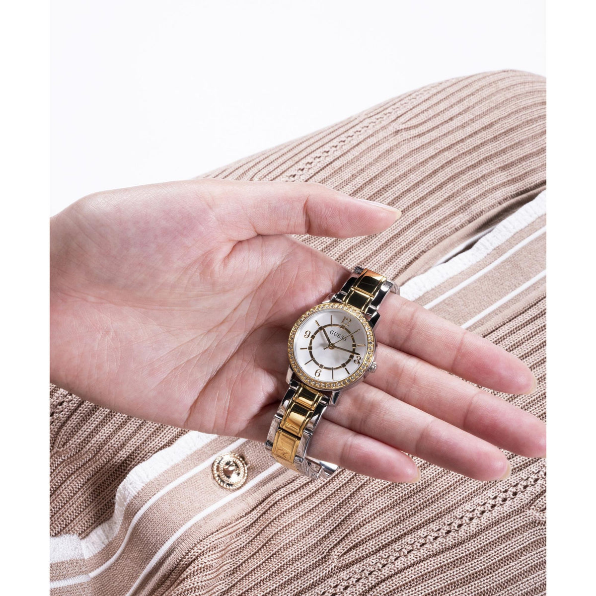 GUESS two-tone analog watch with white dial and gold-and-silver link bracelet on hand