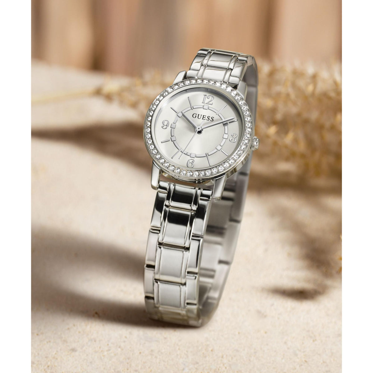 Silver tone analog watch on wrist with white dial and rhinestone bezel