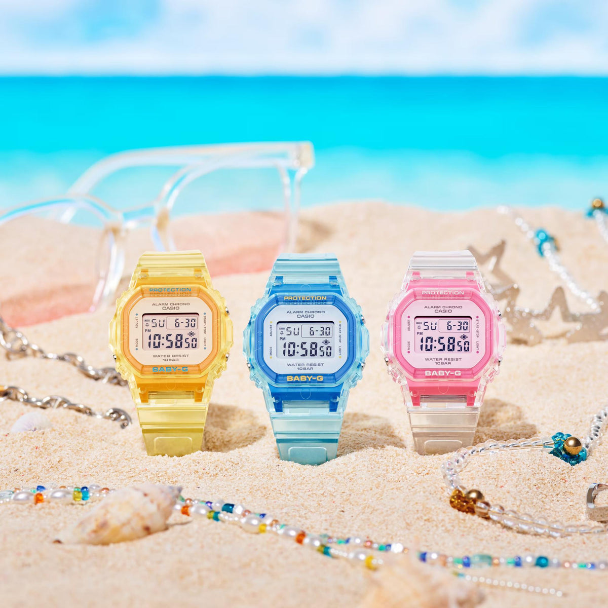 Three translucent jelly digital watches on sand: yellow, blue, and pink resin straps