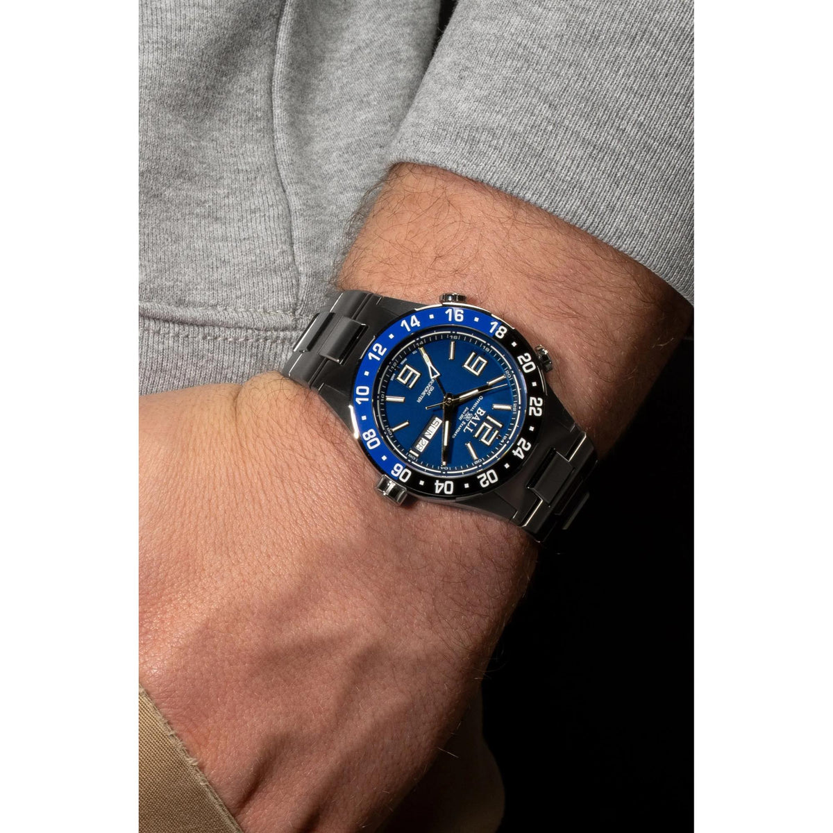 Men's blue dial wristwatch on arm, black bezel and steel bracelet