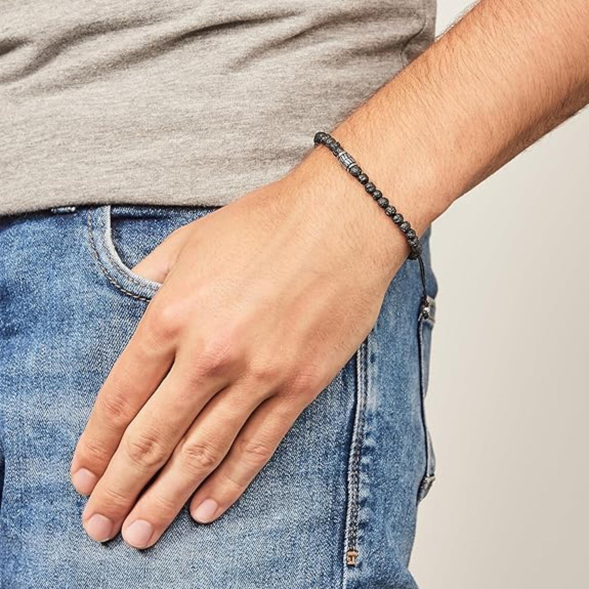 Men's black bead bracelet on wrist with grey shirt sleeve and denim jeans