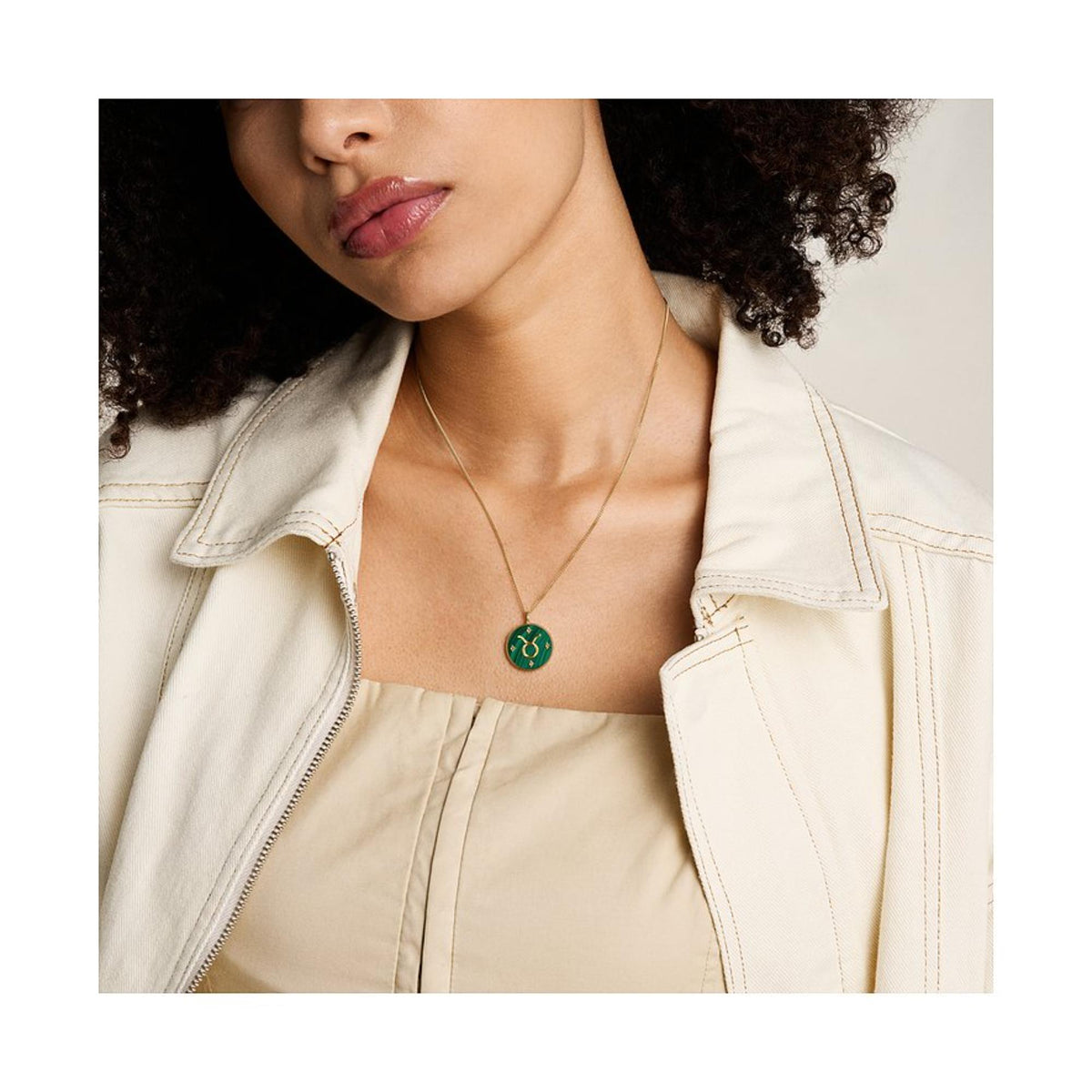 Gold-tone Taurus pendant necklace with green round charm worn on thin chain