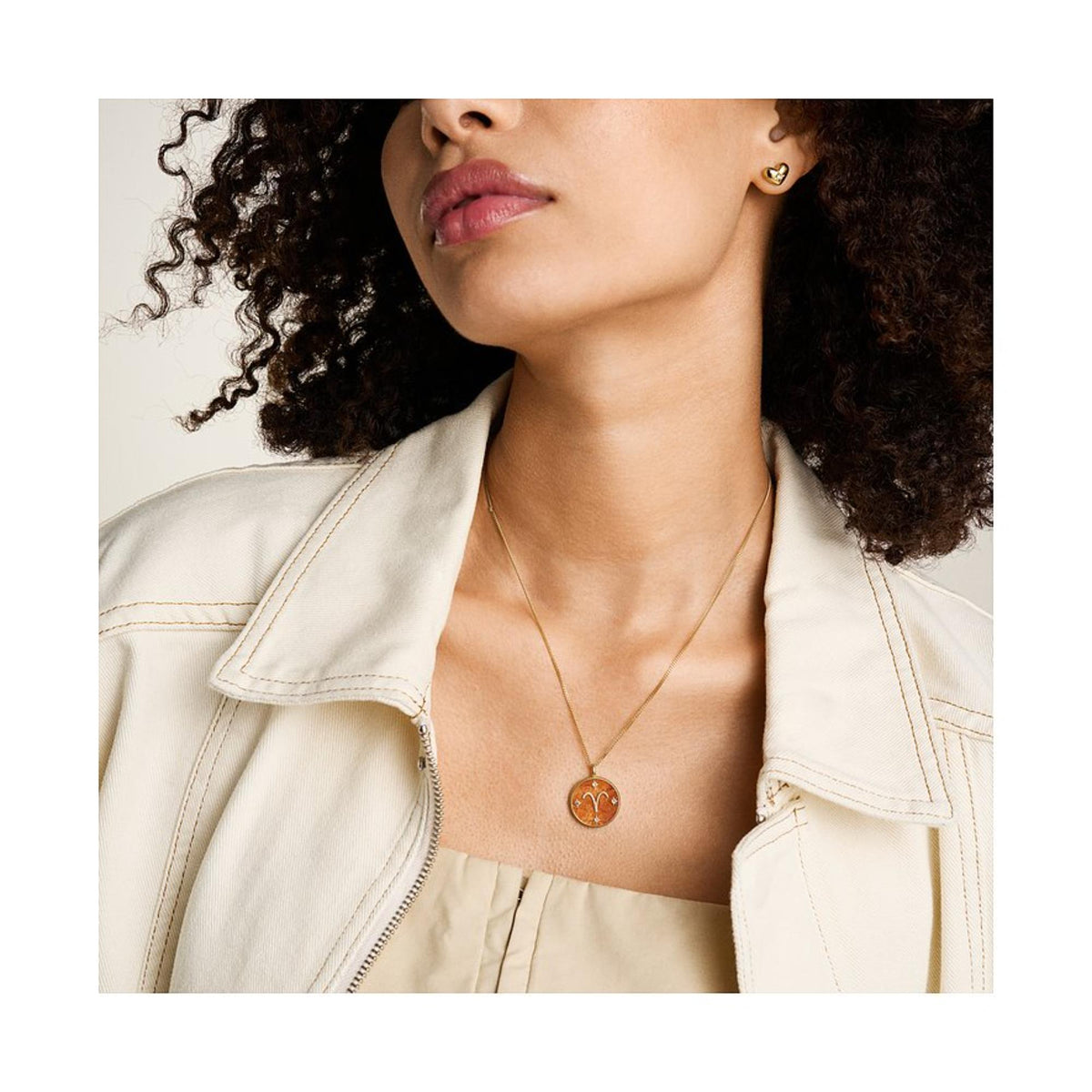 Gold-tone Aries pendant necklace worn on neckline, orange carnelian round pendant