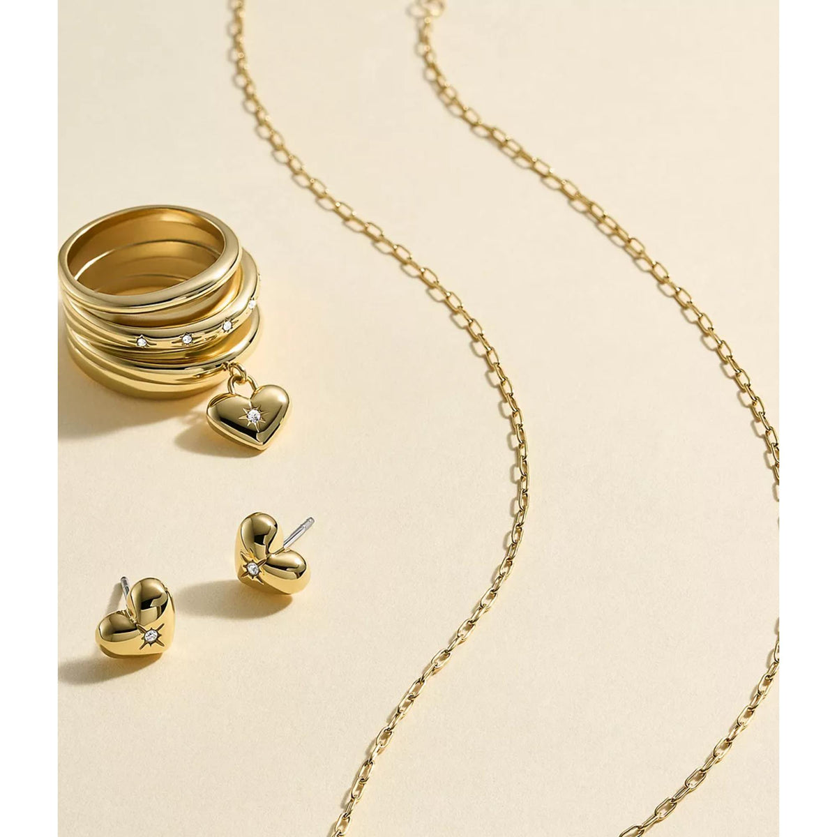 Gold-tone heart stud earrings with dangling charm detail, shown on jewelry display