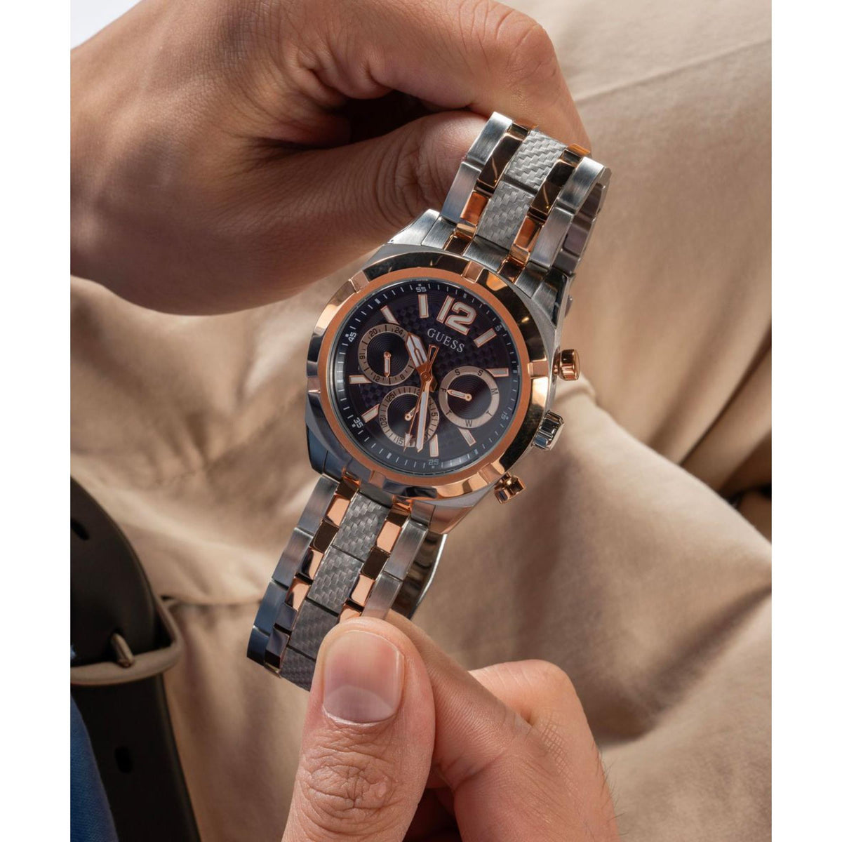 Men's stainless steel watch with blue dial and rose-gold bezel, two-tone bracelet being adjusted.