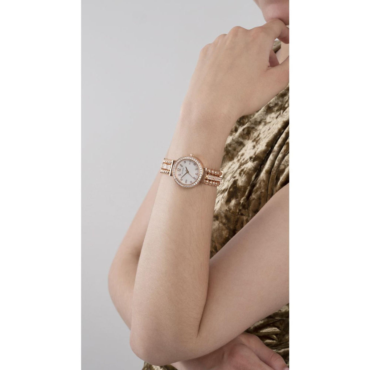 Women’s gold-tone watch on wrist with white dial, crystal bezel, and beaded bracelet strap