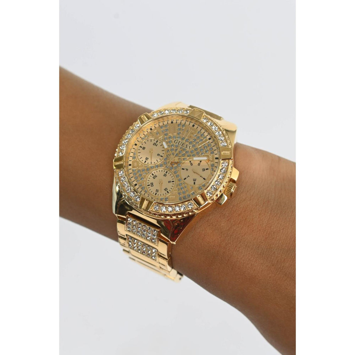 Gold multi-dial watch with rhinestone bezel on wrist, champagne face close-up.