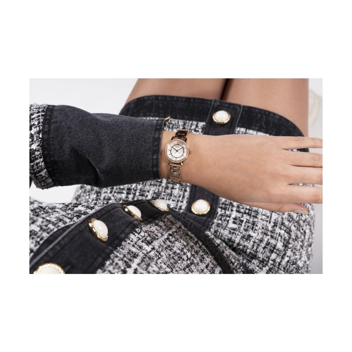 Women’s gold-tone wristwatch with white dial and rhinestone bezel on the wrist.