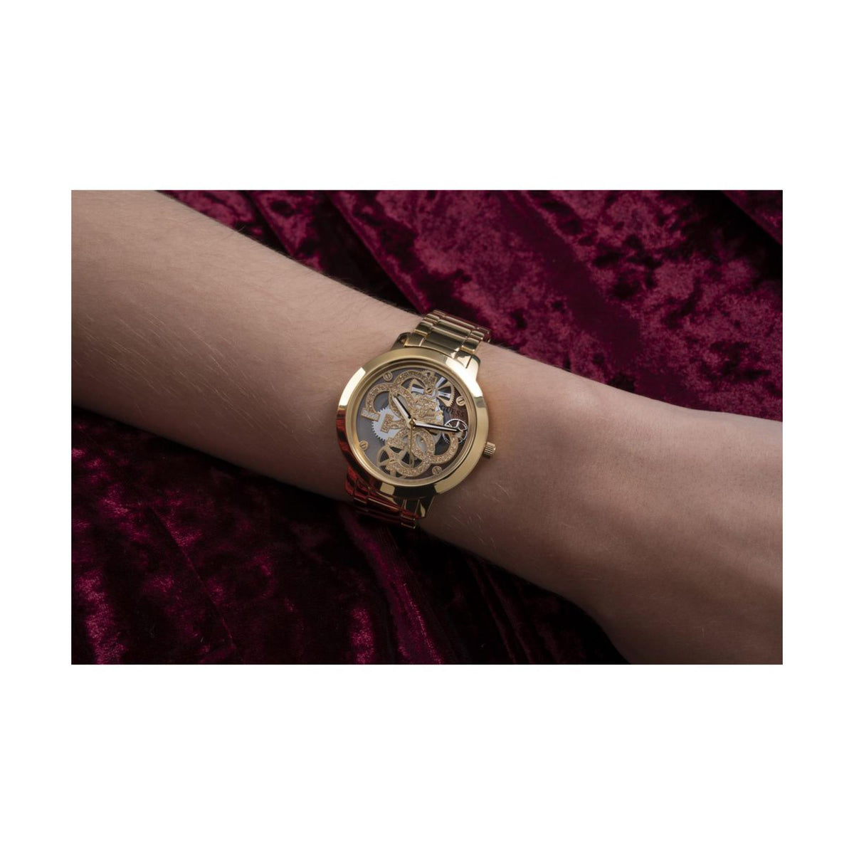 Gold-tone skeleton dial watch on wrist with round case and metal link bracelet