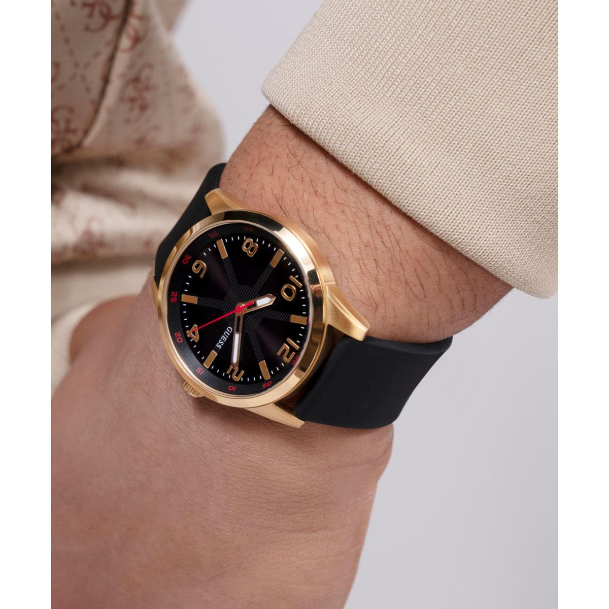 Men’s wristwatch on wrist: black dial, gold-tone case, red indices, black silicone strap.