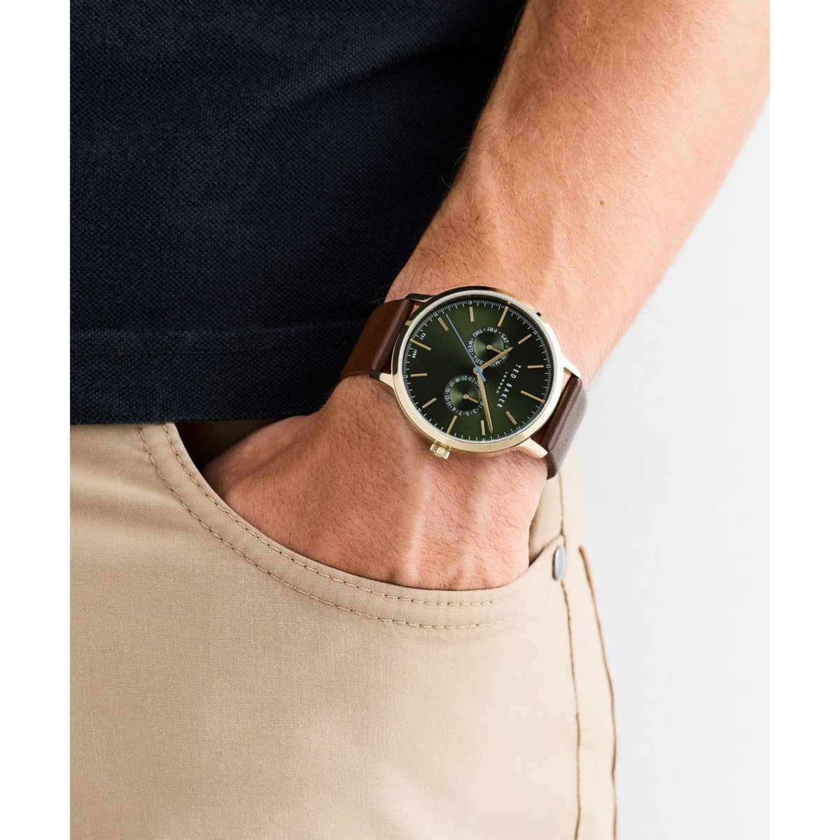 Men's wristwatch with dark green dial and brown leather strap, worn on forearm, gold-tone case