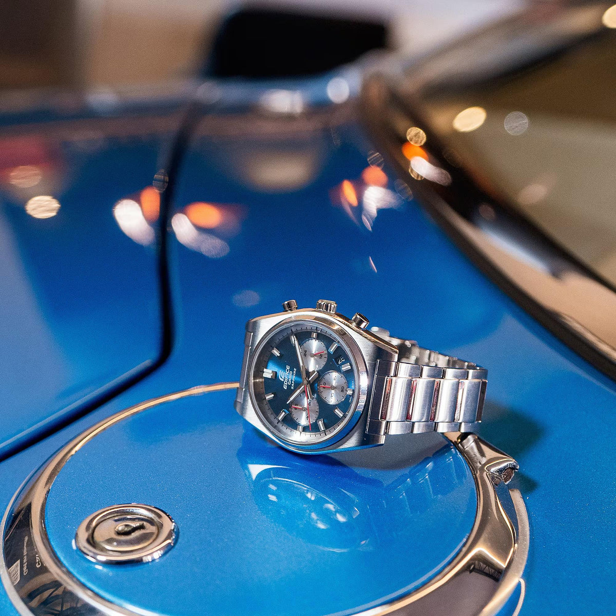 Men's stainless steel chronograph watch with blue dial, angled side view on vehicle
