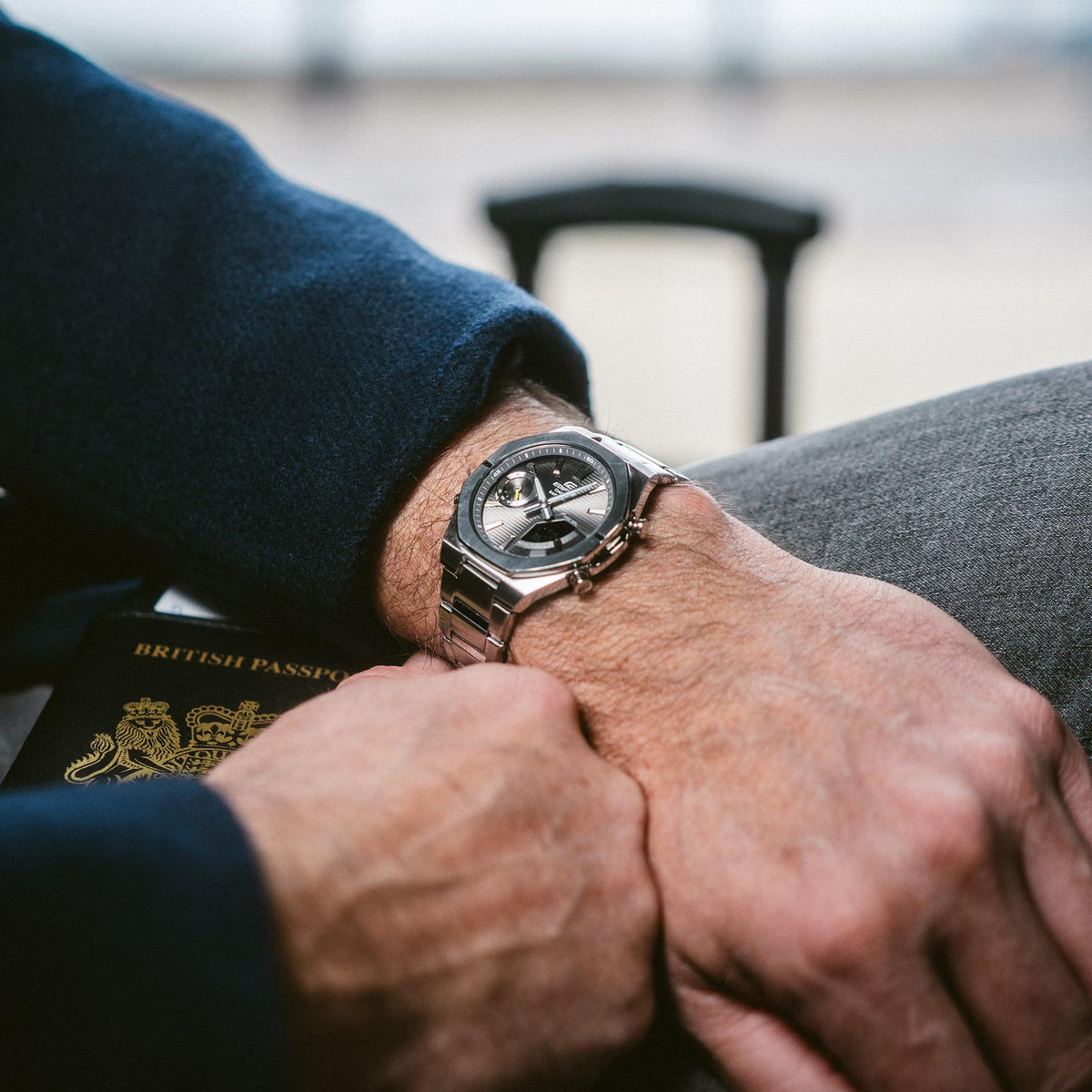 Men's wristwatch with dark dial and metal case on a hand near a coat sleeve.