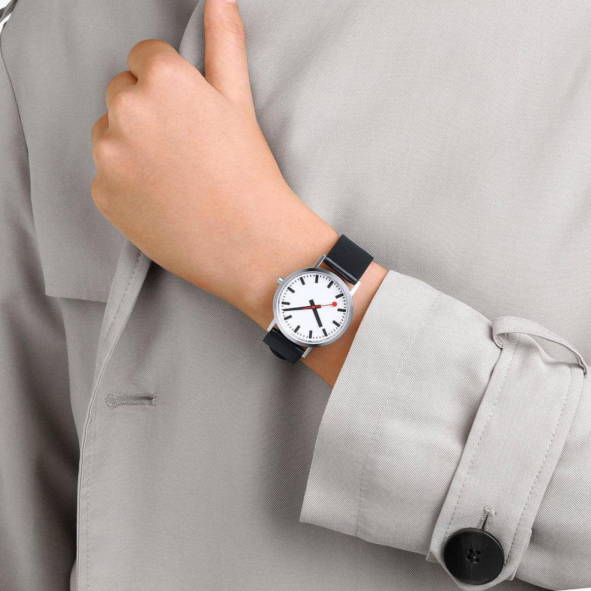 Women's wristwatch worn with white shirt sleeve, white dial with red details and black strap