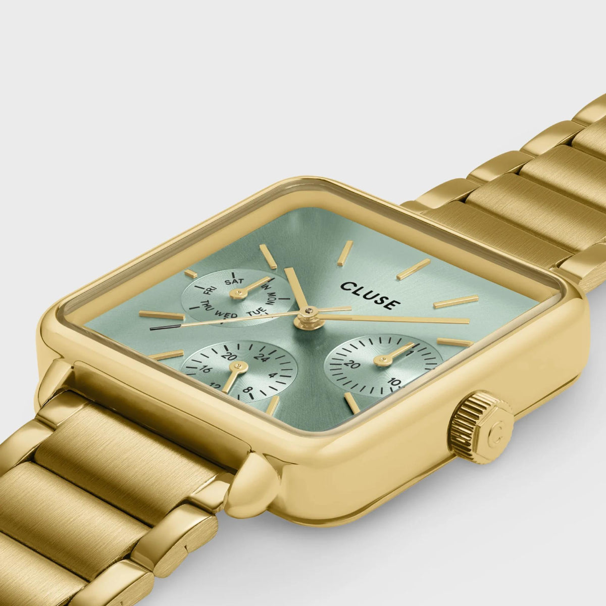 Angled close-up of gold-tone square chronograph watch with light green dial and metal strap