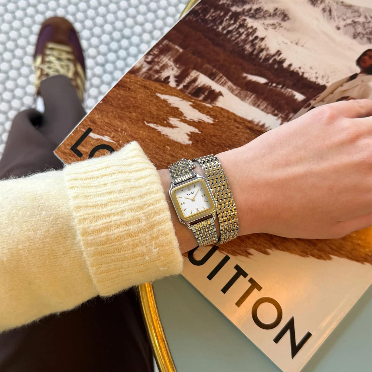 Square quartz watch with two-tone mesh band on wrist near shopping bag