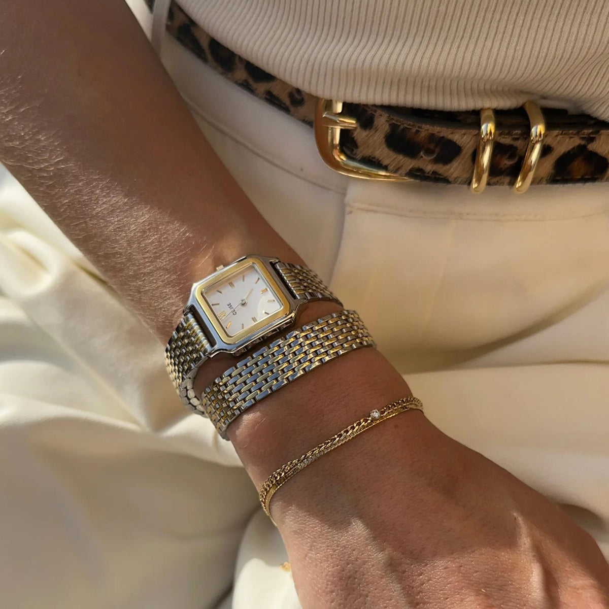 Square quartz watch with gold markers on woven metal mesh strap on wrist