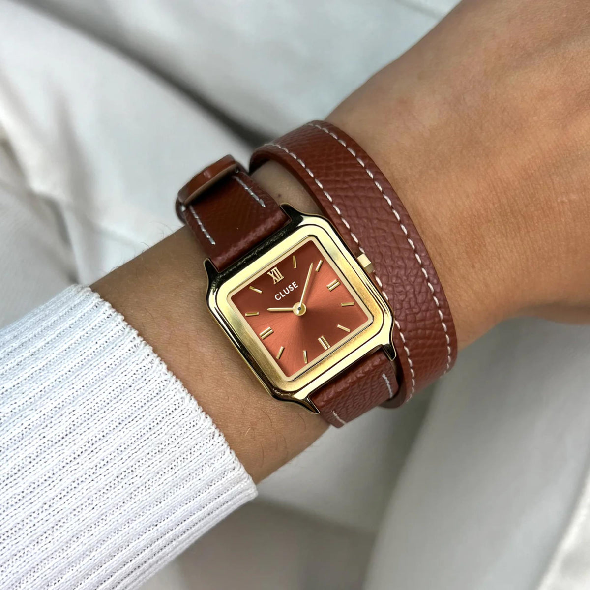CLUSE square watch on wrist, brown leather strap and reddish dial with Roman numerals
