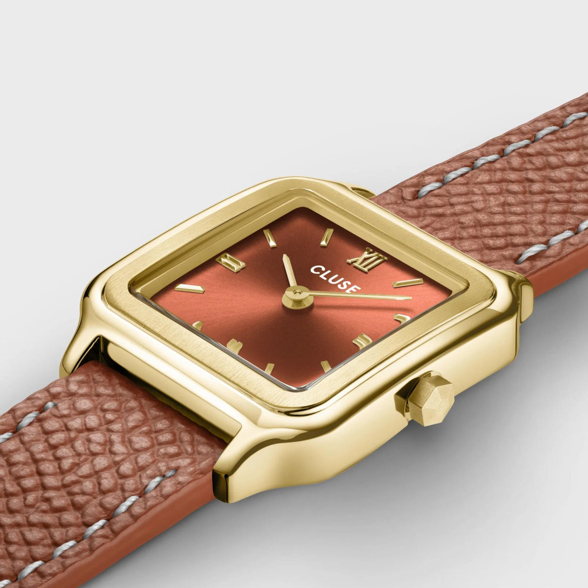 Close-up of CLUSE square watch with gold-tone case and brown leather strap; Roman dial