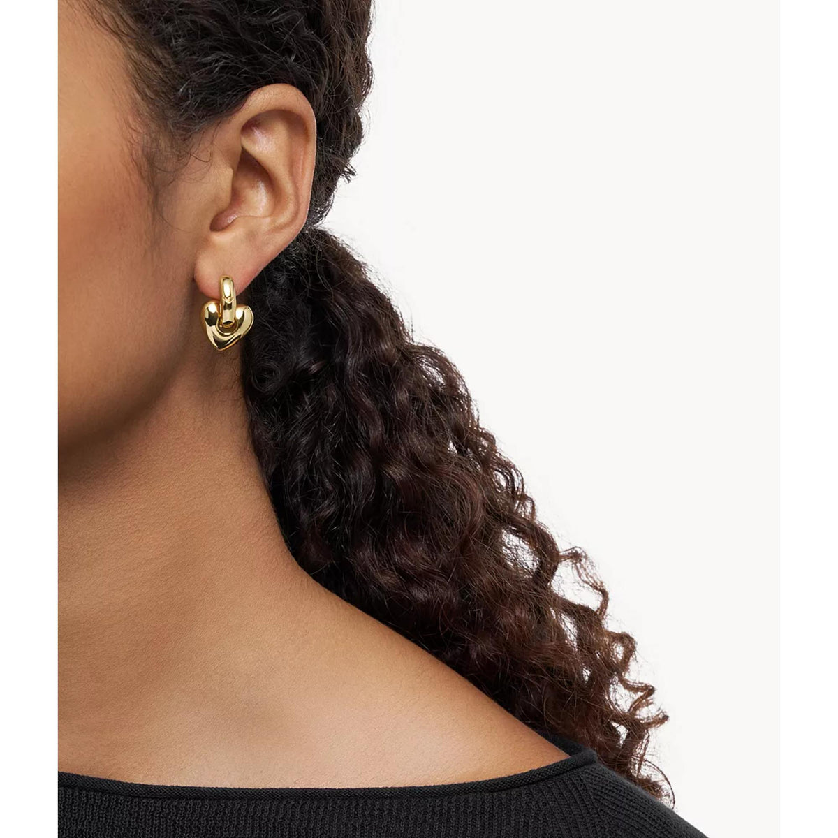 Gold-tone heart hoop earring on ear with polished heart front and hinge
