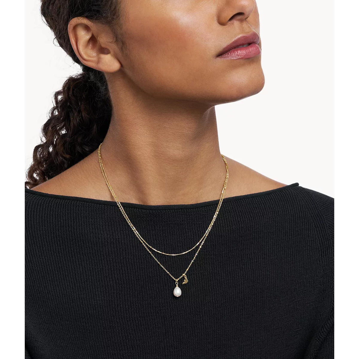 Gold-tone layered pendant necklace on neckline: round medallion charm and pearl drop