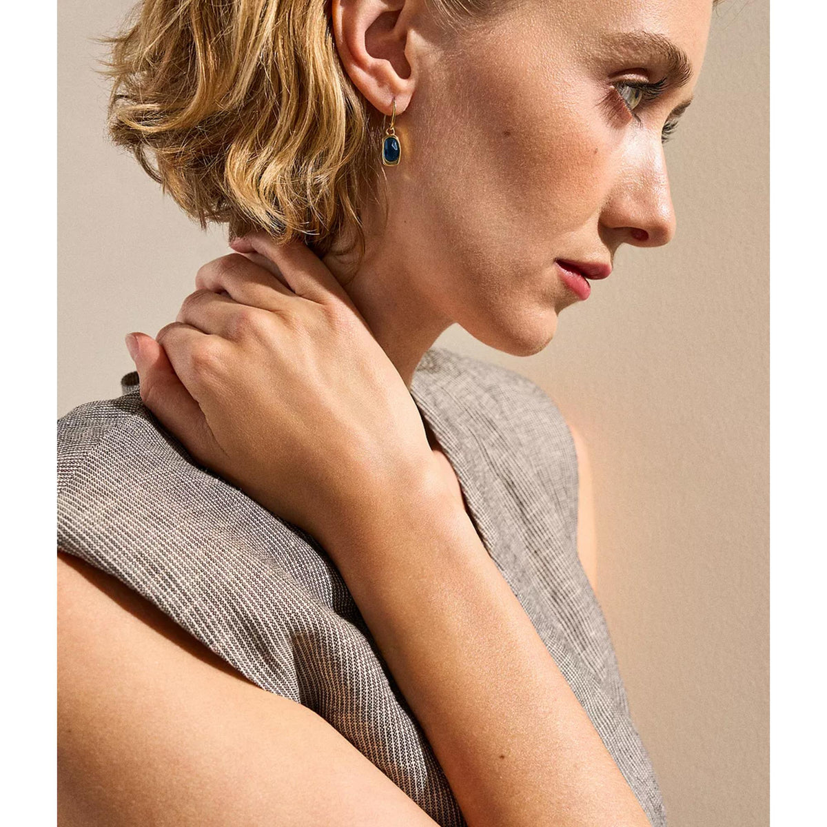 Gold-tone drop earrings with oval blue stone, seen in profile on model.