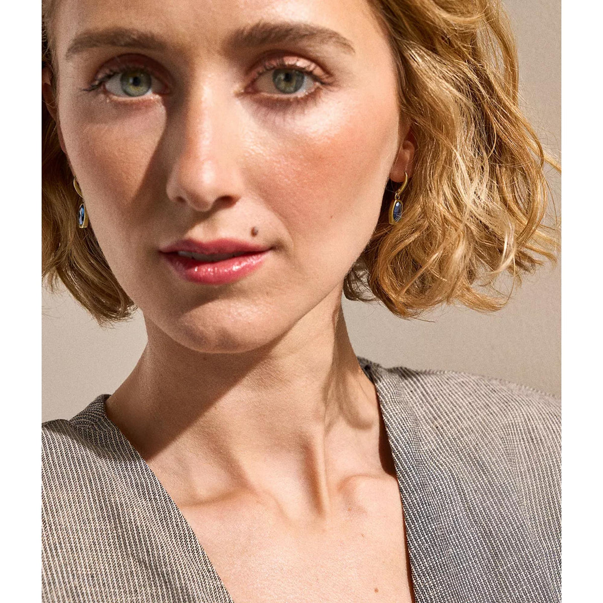 Gold-tone drop earrings with blue oval stones on model, close-up around face and neck.