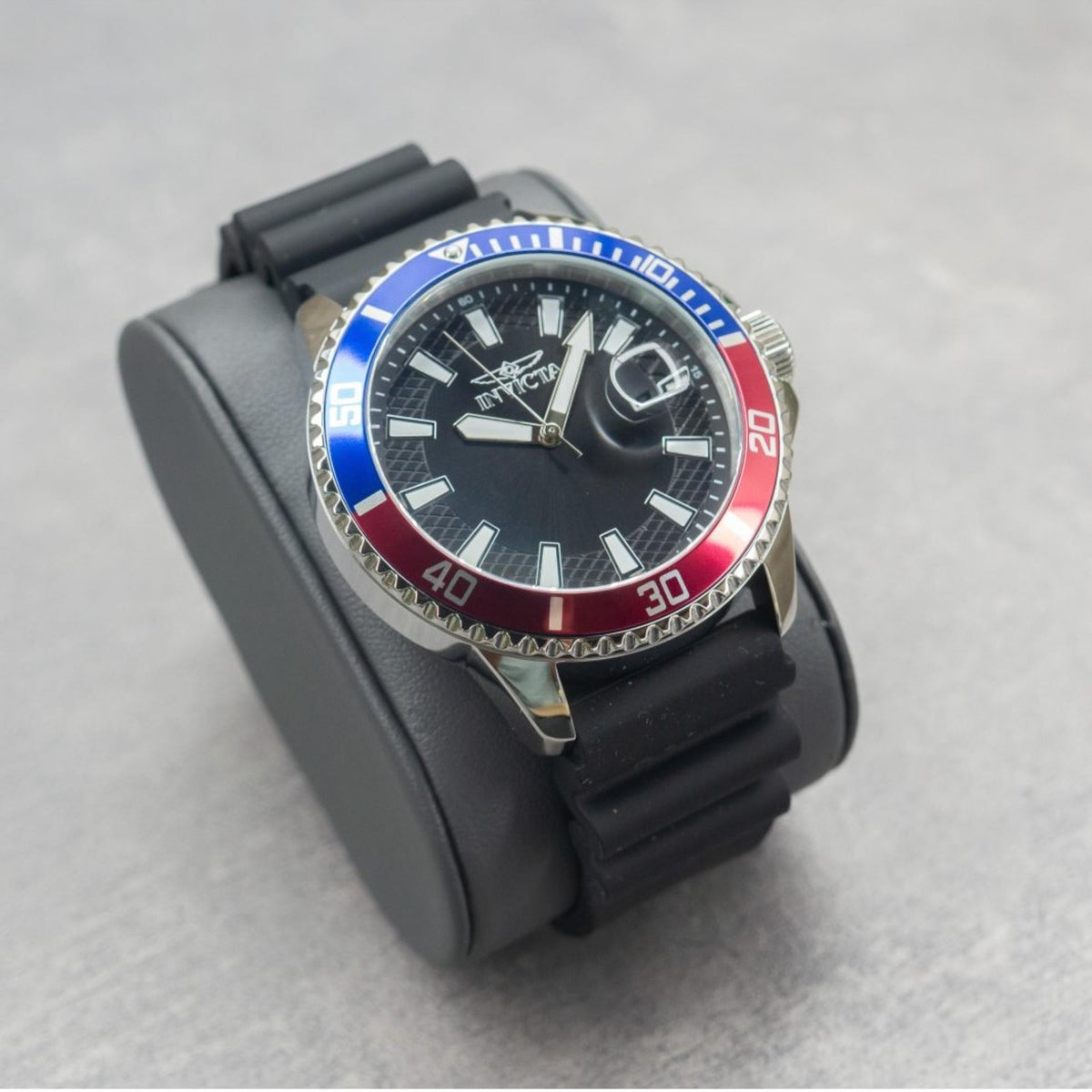 Men's dive watch close-up: black silicone strap, black dial, blue-red bezel ring.