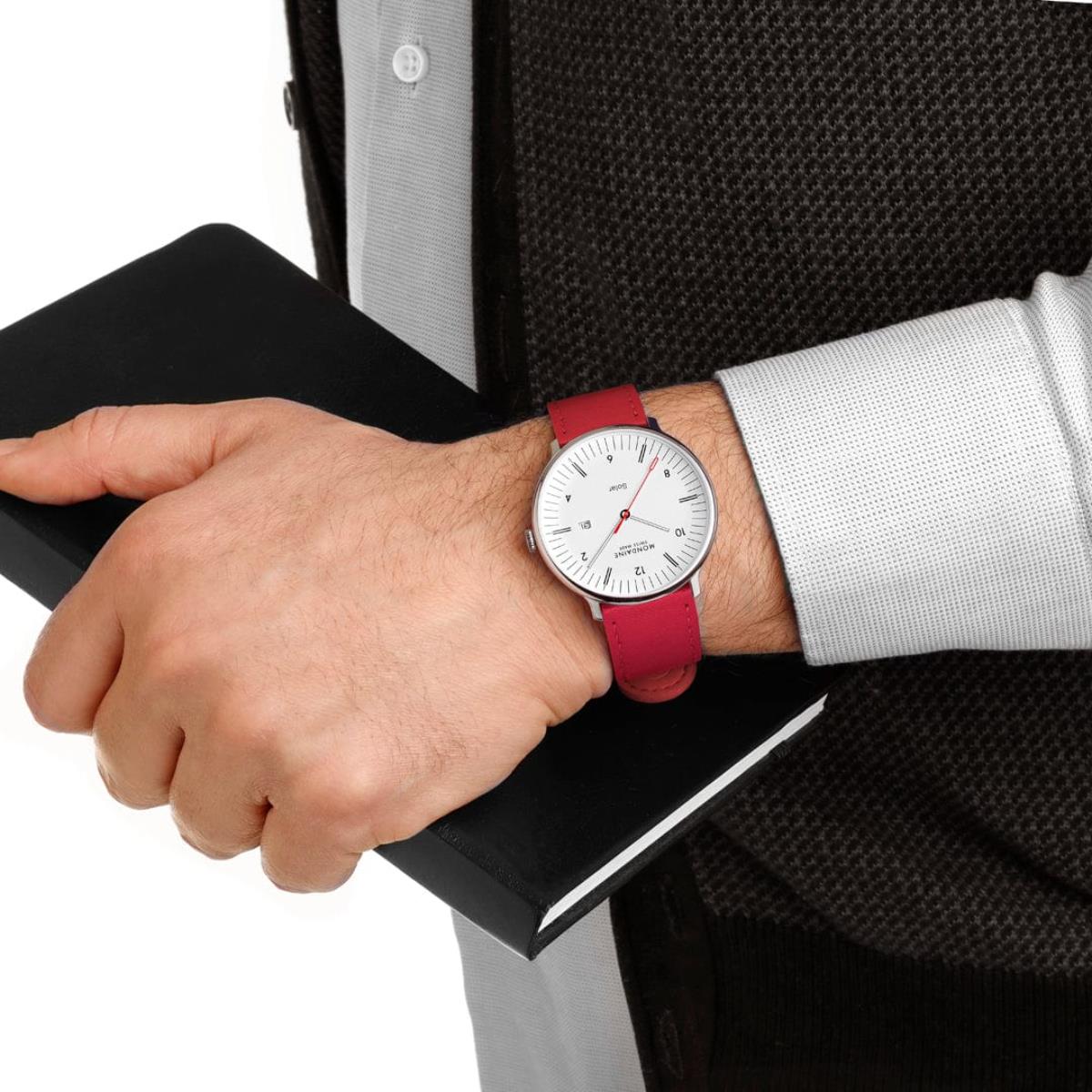 On-wrist view of a man holding a black notebook, wearing the Mondaine  Doppio MLE.41910.LCV solar watch with a red vegan grape strap