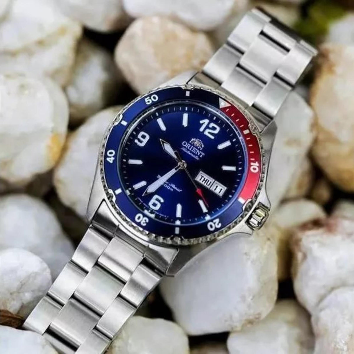 Men's automatic watch with blue dial, red bezel ring, steel bracelet on stones