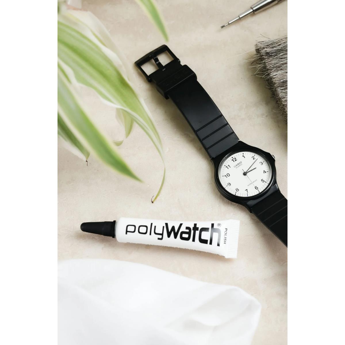 Acrylic plastic scratch remover polish tube with applicator tip next to black wristwatch.