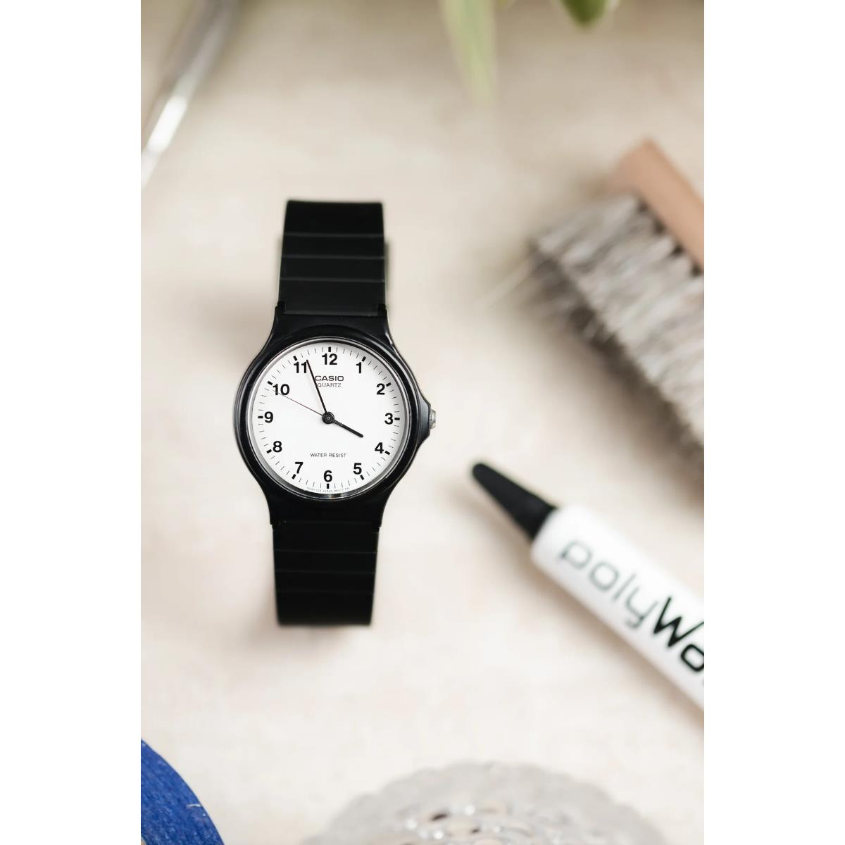 Black wristwatch with white dial and black strap, with polish tube partially visible.