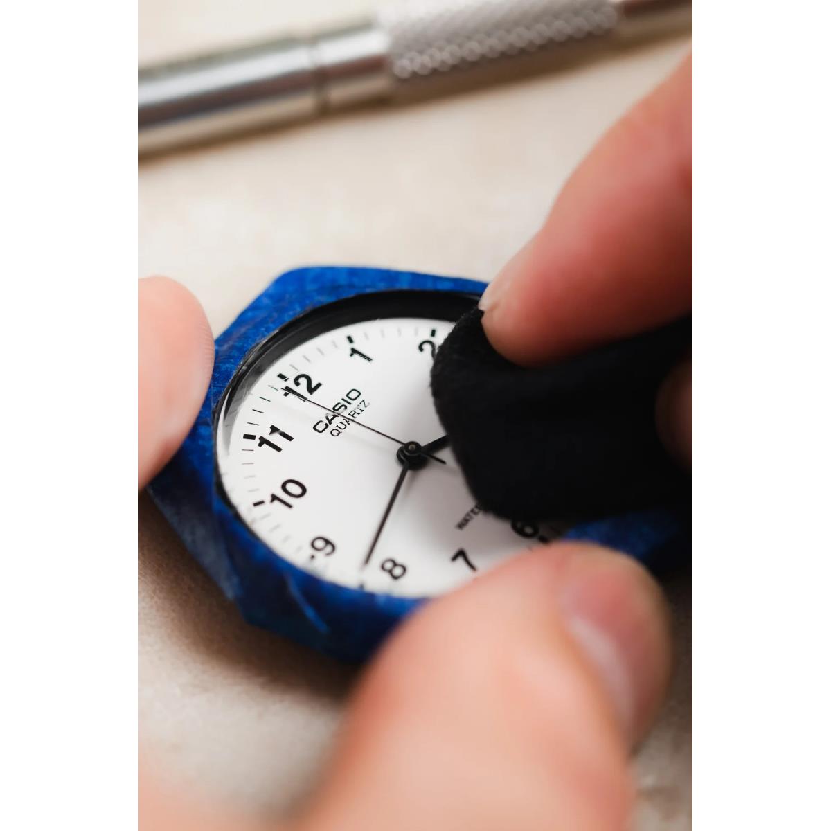 Black wristwatch being rubbed by fingers on blue polishing pad.