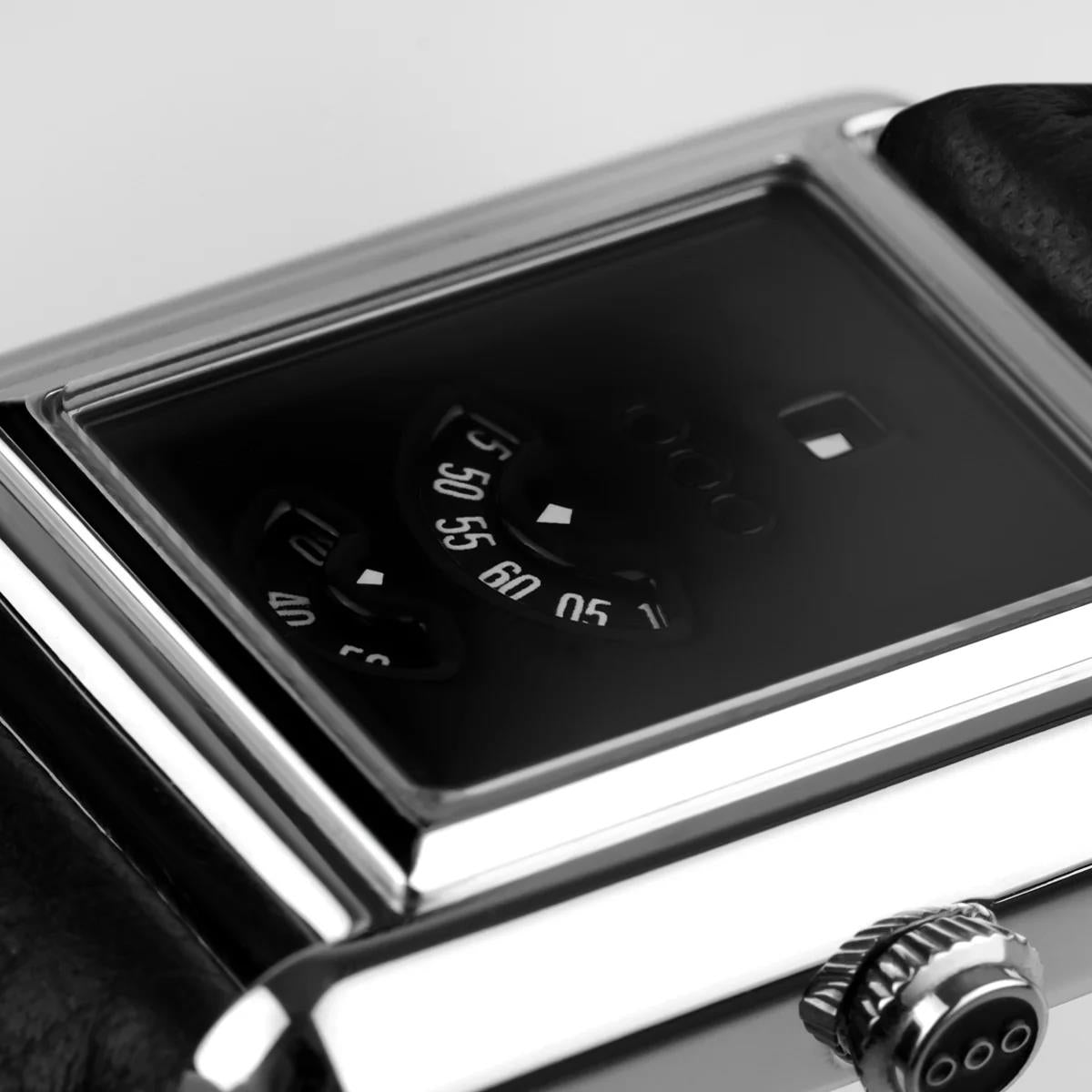 Close-up of black dial with hour markers and date display on rectangular silver-tone case