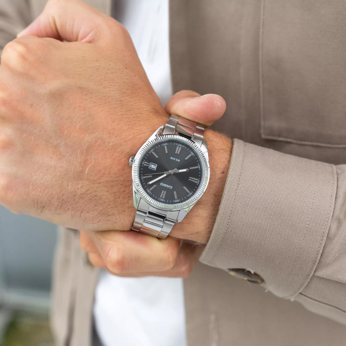 Casio Collection MTP-1302PD-1A1VEF on a person's wrist, highlighting the stainless steel link bracelet and classic round case paired with a casual tan shirt