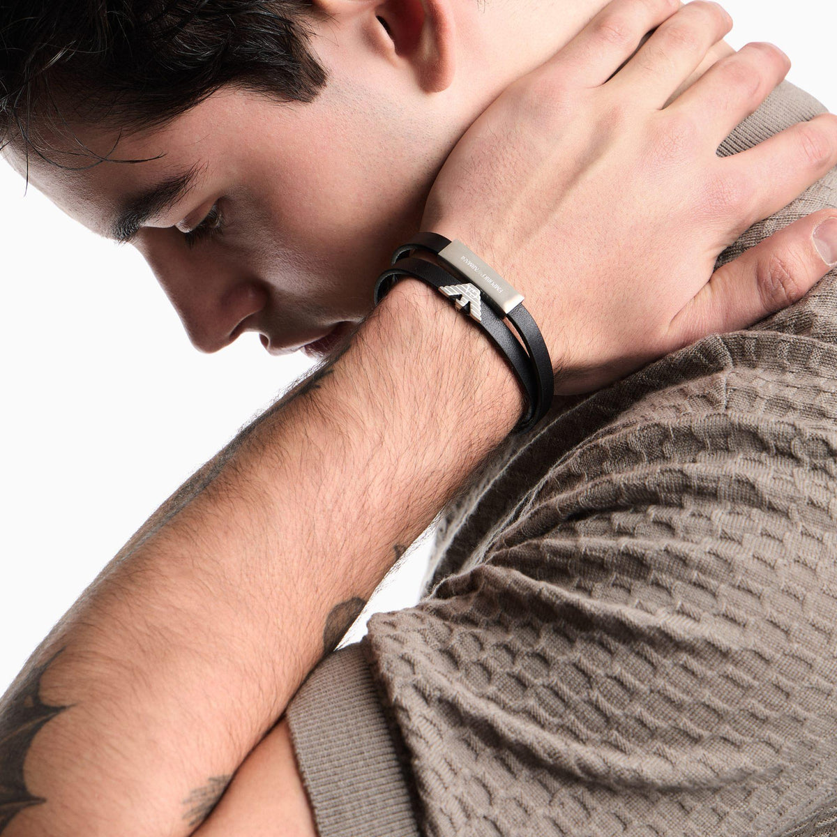 Black leather bracelet on wrist with silver-tone clasp and ID plate