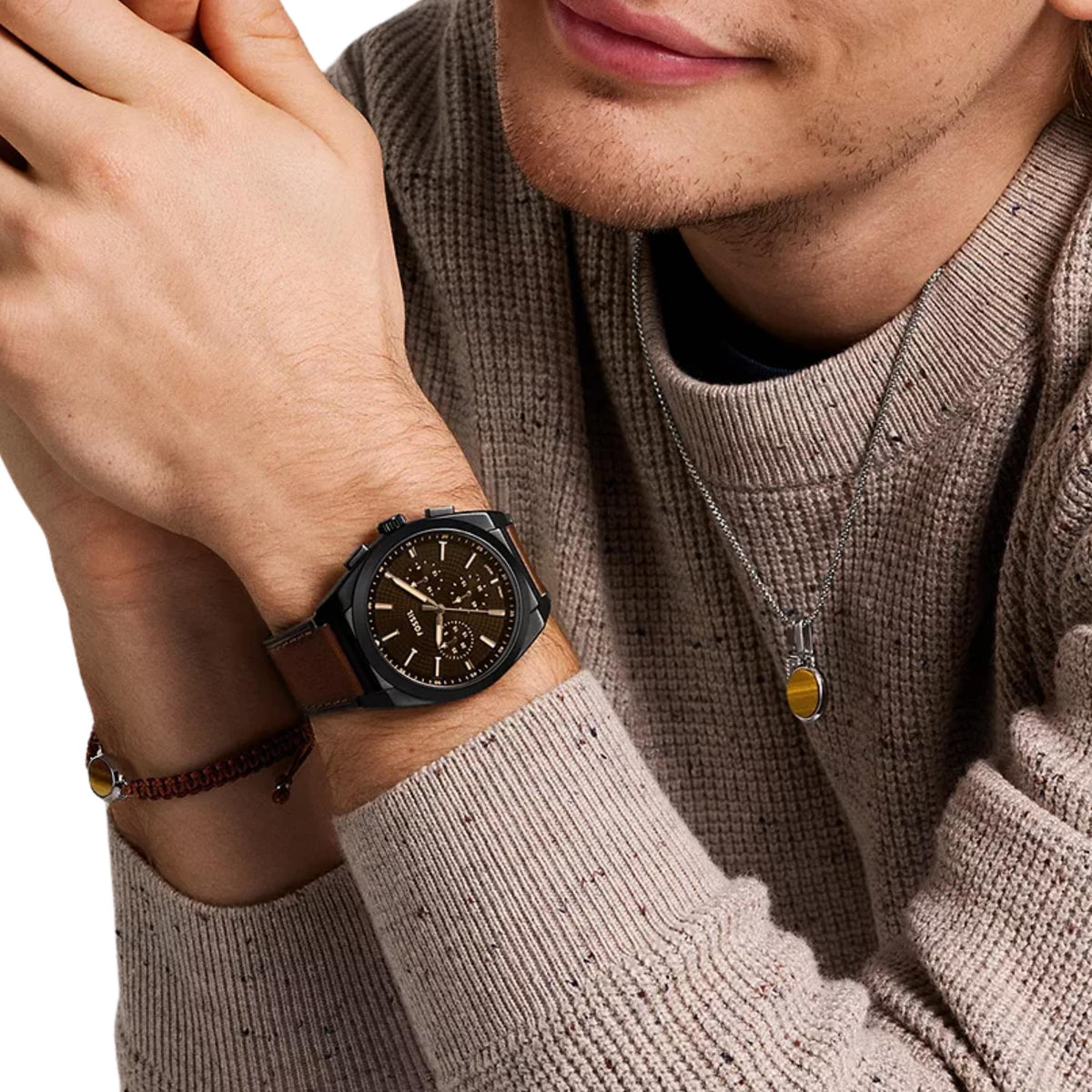 Mens chronograph watch on wrist with brown leather band and dark dial