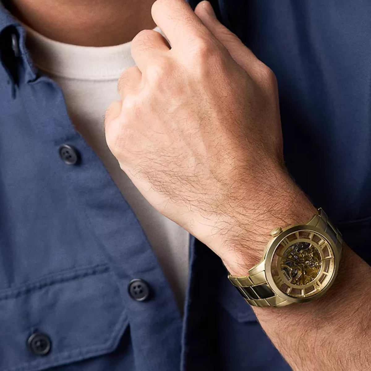 Gold skeleton dial quartz watch worn on man's wrist with metal link bracelet