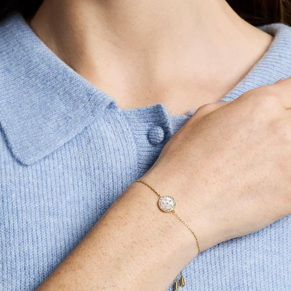 Gold-tone bracelet on wrist with oval mother-of-pearl station charm and crystal bezel