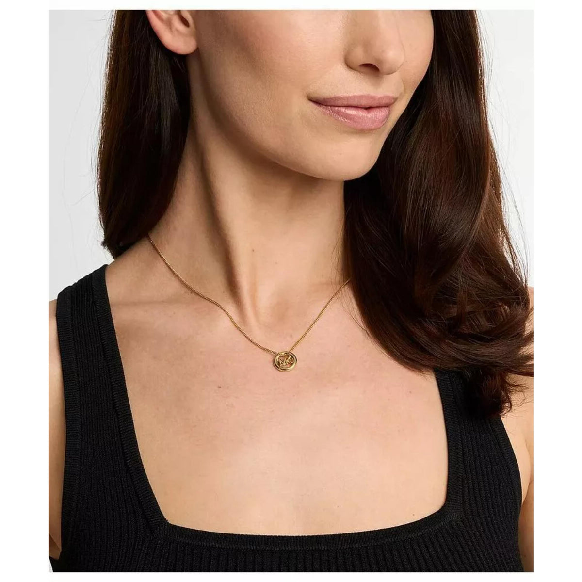 Gold tone round pendant necklace worn close-up, MK logo medallion