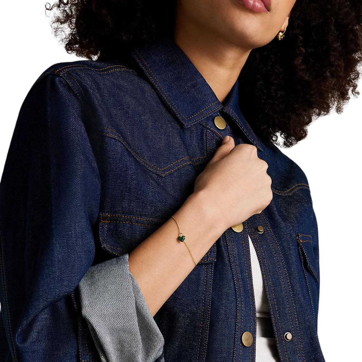 Gold-tone bracelet with small green heart charm on wrist