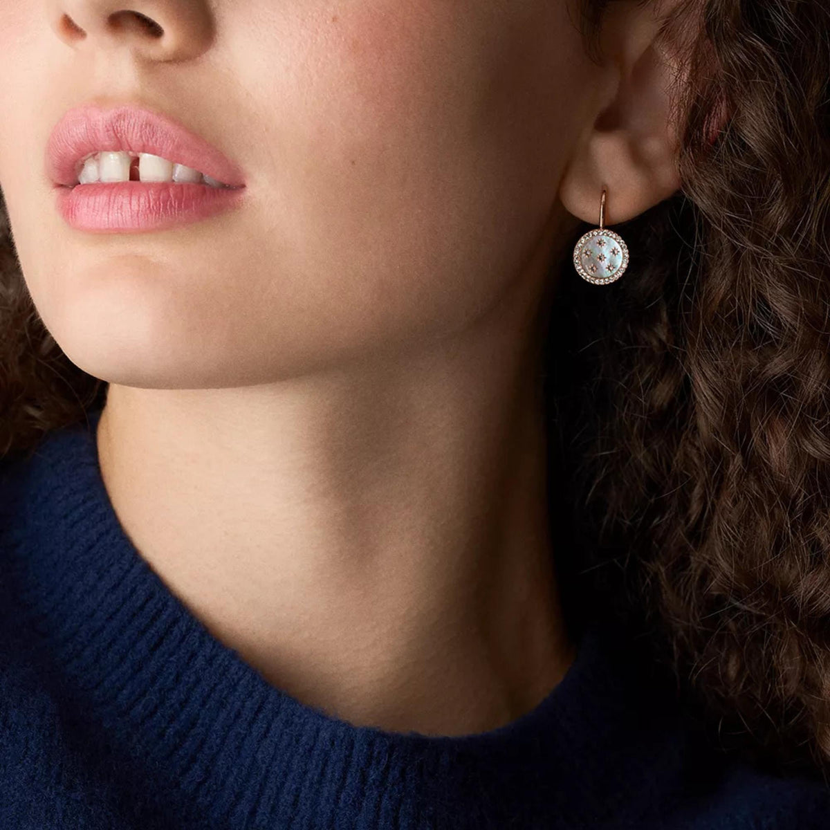 Model wearing oval blue iridescent drop earrings with crystal halo and rose gold hooks.