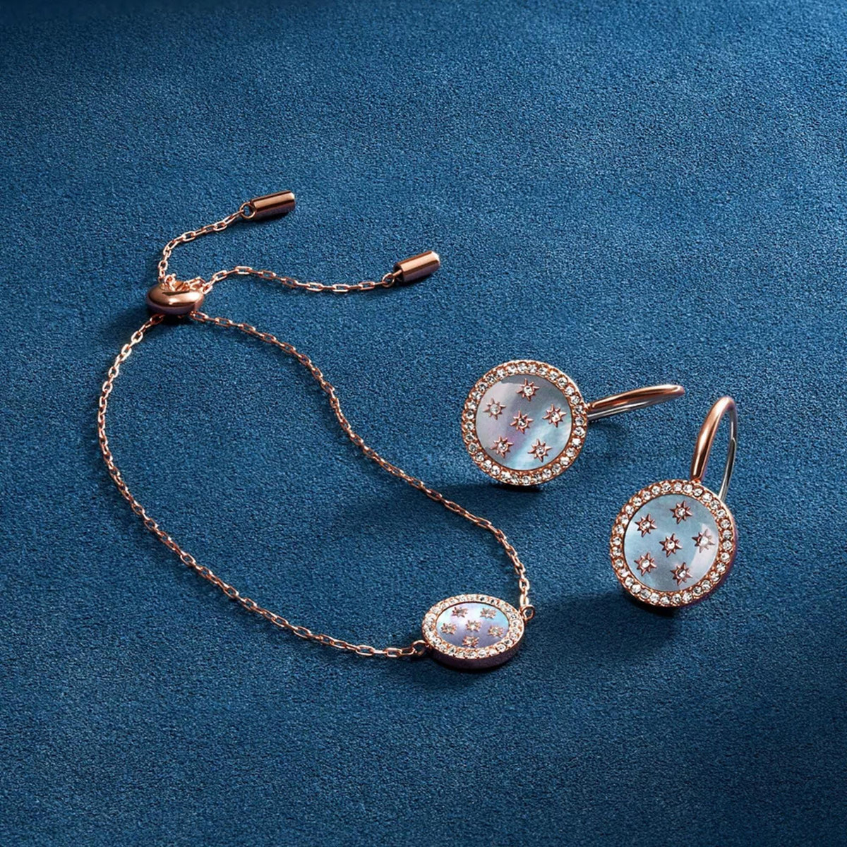 Oval blue iridescent drop earrings with crystal border and star-like details, rose gold hooks.