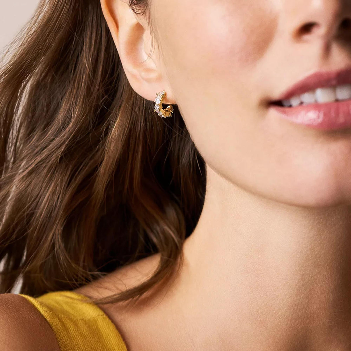 Gold-tone hoop earrings with mixed shape clear crystals, close-up on ear