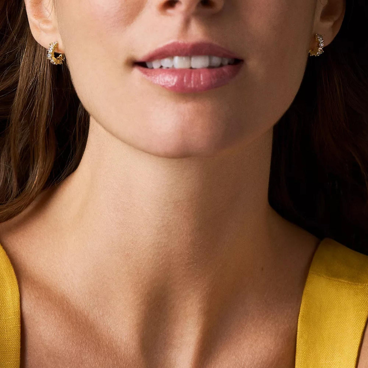 Gold-tone hoop earrings with mixed clear crystals, close-up near neckline