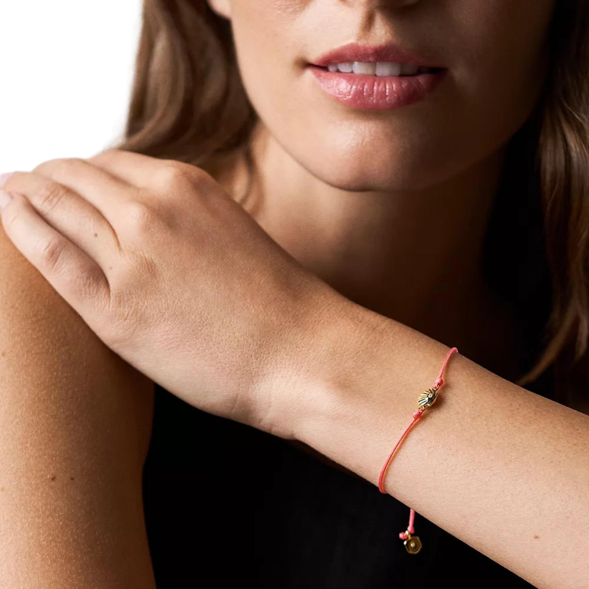 Gold-tone seashell bracelet on wrist with coral braided cord and charm dangles